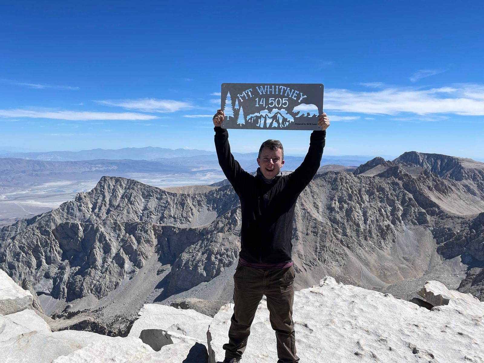 Adam Moeller on the summit of Mount Whitney, holding the 14,505 foot summit sign above the Sierra Nevada