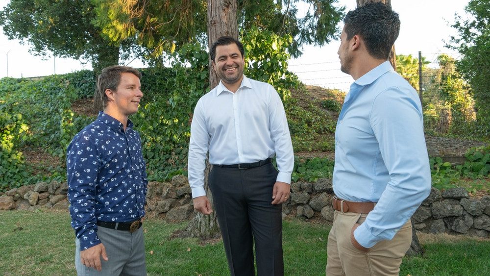 Three men in tucked dress shirts laughing together outdoors